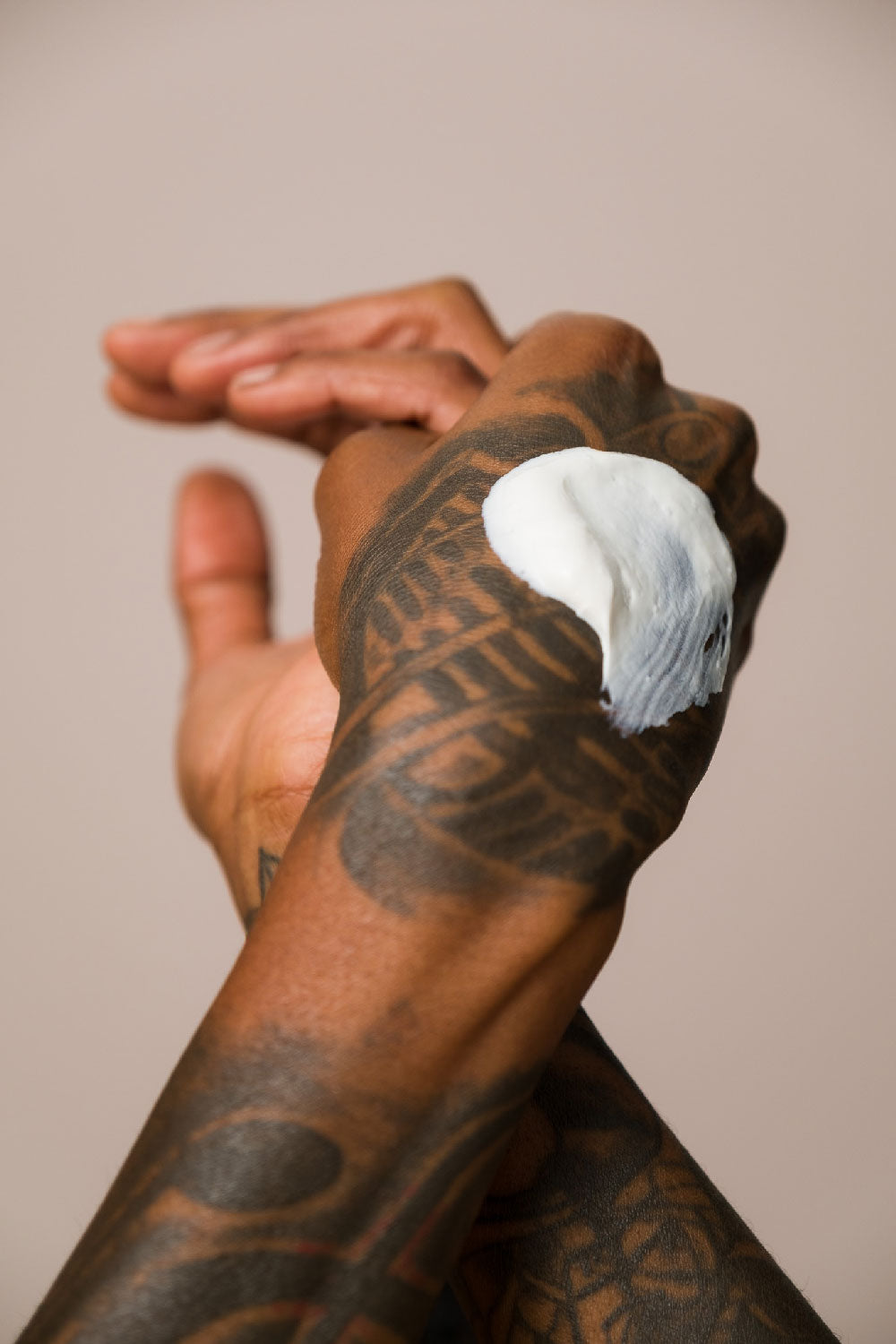 Two tattooed hands entwined, with a swipe of DAILY HABIT SPF 30 on the top of one hand, against a khaki background.