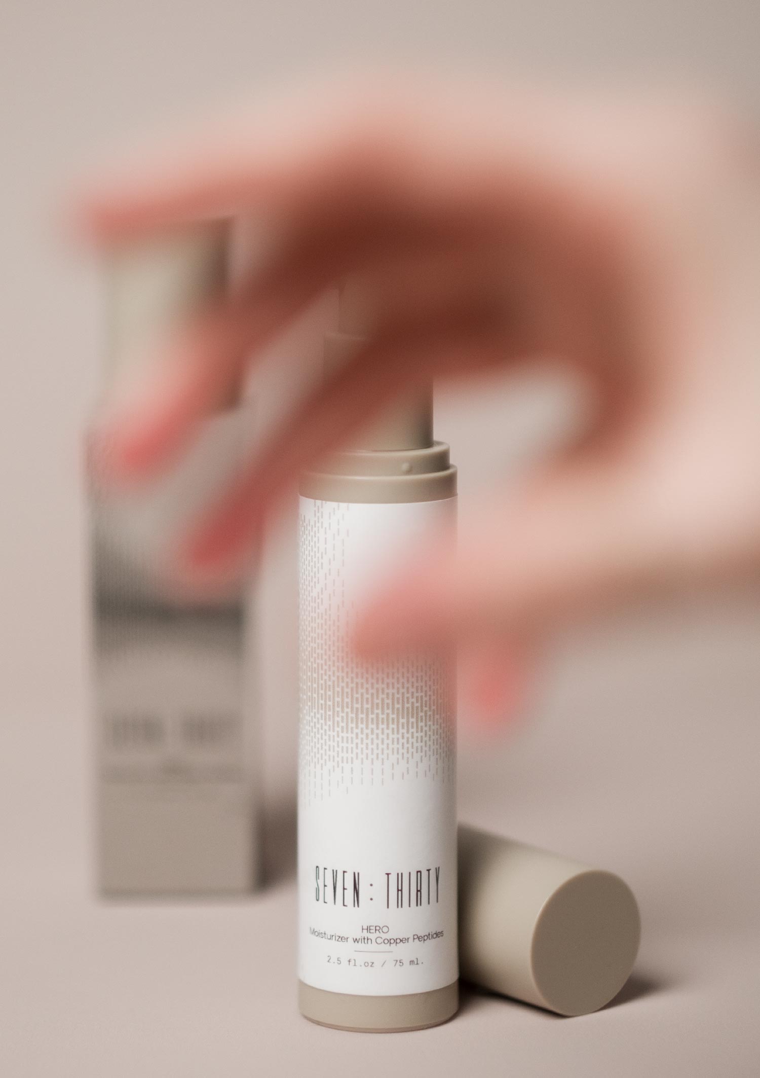 HERO Moisturizer with Copper Peptides on a khaki background with an out-of-focus hand in the foreground